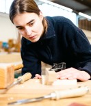 Foto: Frau über einen Tisch gebegt und mit Holz arbeitend