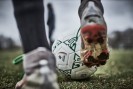 Großaufnahme eines Fußballschuhs mit roter Sohle, der gegen einen Fußball tritt
