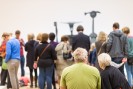 Foto: Rückenansicht einer Menschengruppe, die einer Skulpturengruppe zugewandt ist.