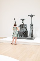 Foto: Frau in buntem Kleid, stehend vor einer Max Ernst Skulptur
