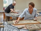Foto: Ein Mann und eine arbeiten an der Restaurierung zweier Werke über einen Tisch gebeugt