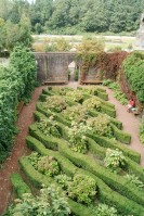 Von einer Mauer umfasster Bereich eines Parks. In der Mitte befinden sich wellenförmige Hecken. Im Hintergrund Parklandschaft. Innerhalb des eingegrenzten Bereichs sitzt ein Mann auf einer Bank.