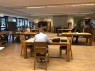 Vier junge Männer schreiben an Tischen. Ihnen gegenüber sitzt ein Mann an einem Tisch. Er ist von hinten zu sehen.