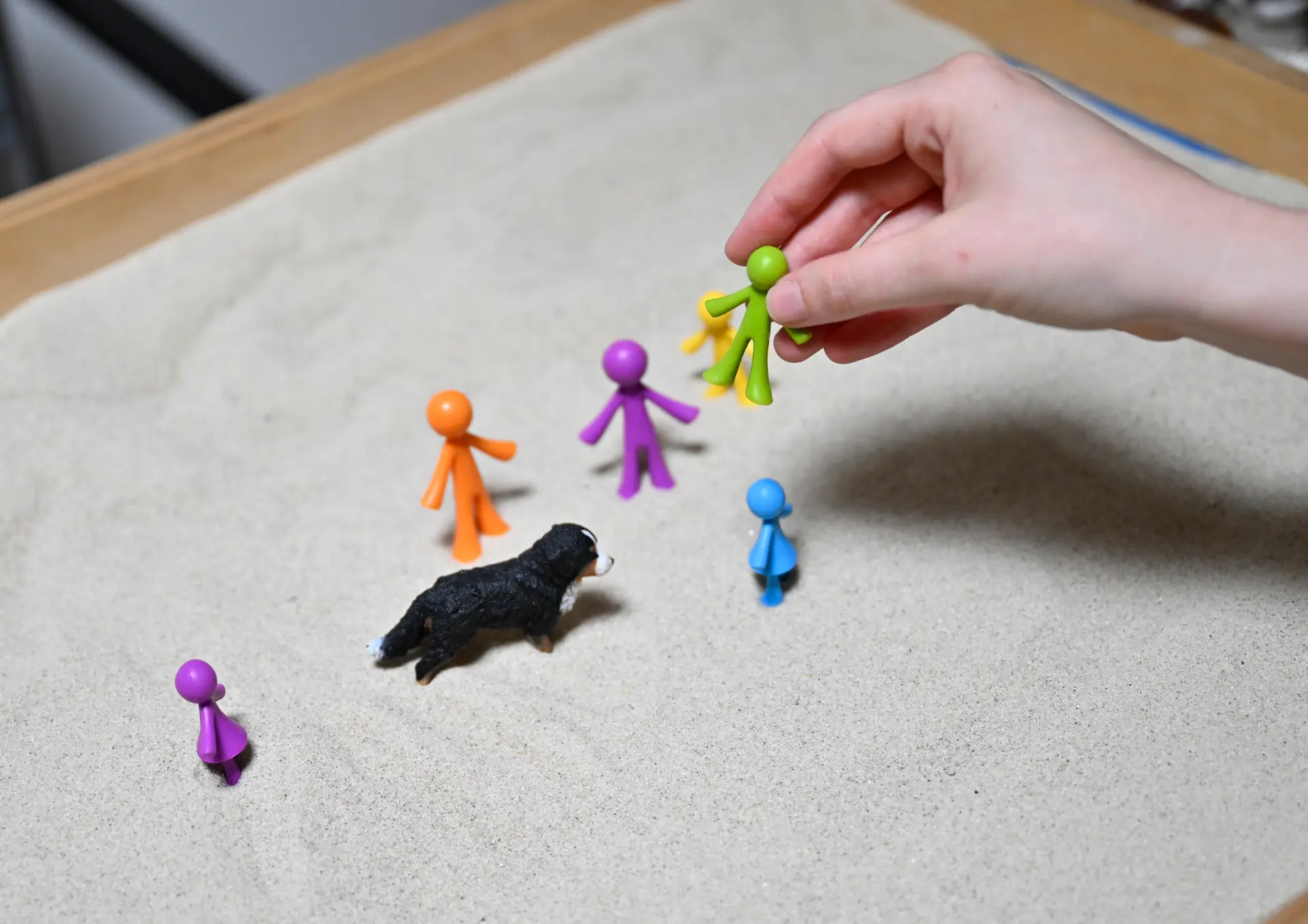 Kleine, bunte Figuren werden von einer Hand aufgestellt.