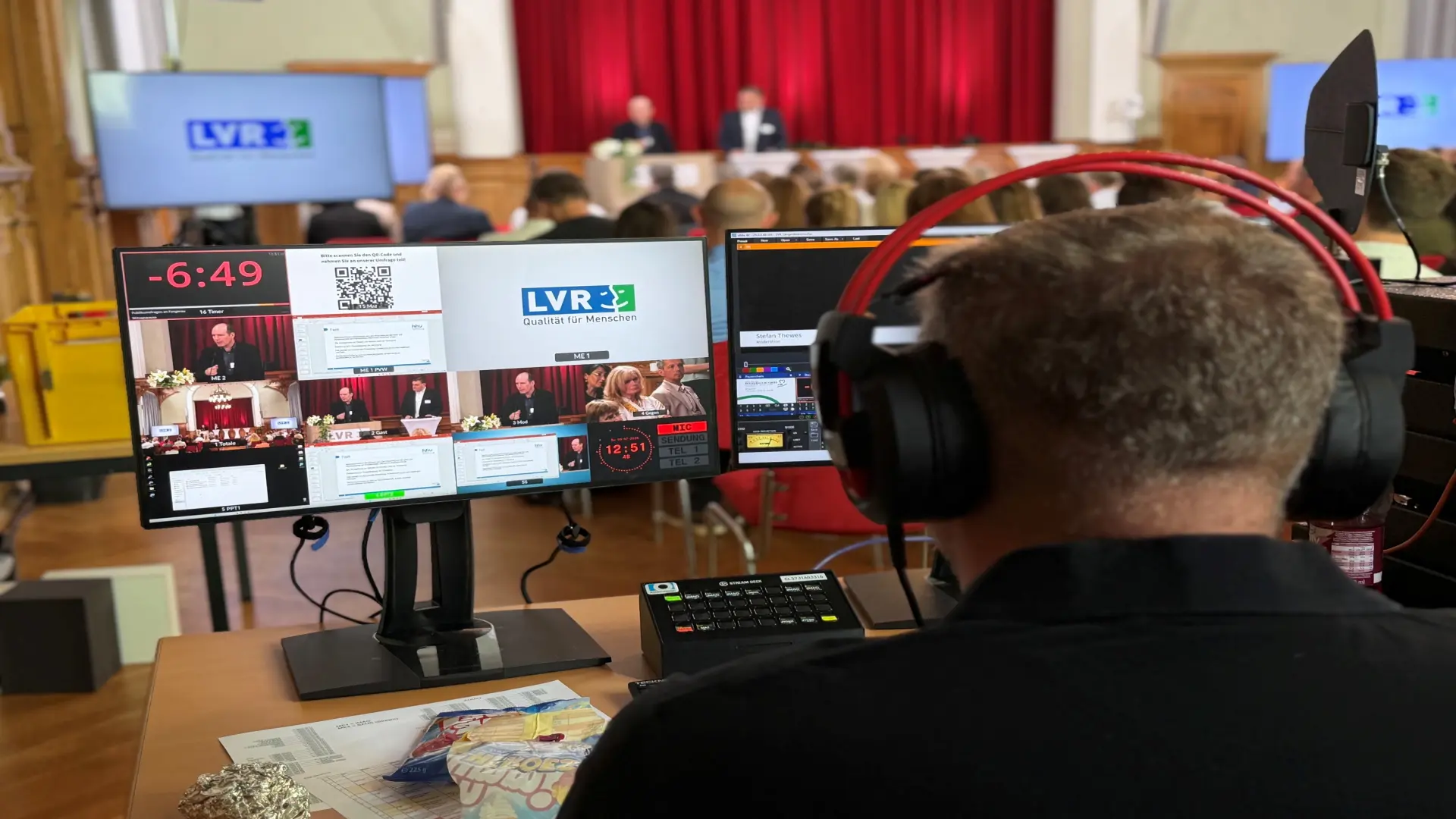 Zu sehen ist eine noch leere Bühne mit einem großen Bildschirm mit einem Willkommensgruß zur Veranstaltung "Der Mensch im Fokus",