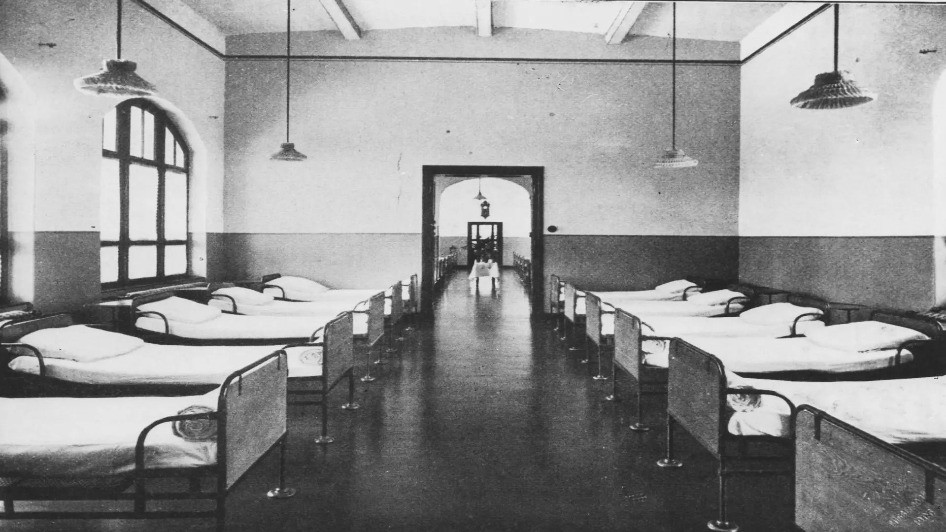 Blick in den Schlafsaal der LVR-Klinik Viersen vor 100 Jahren: ca 10 Betten sind in zwei langen Reihen nebeneinander aufgestellt.