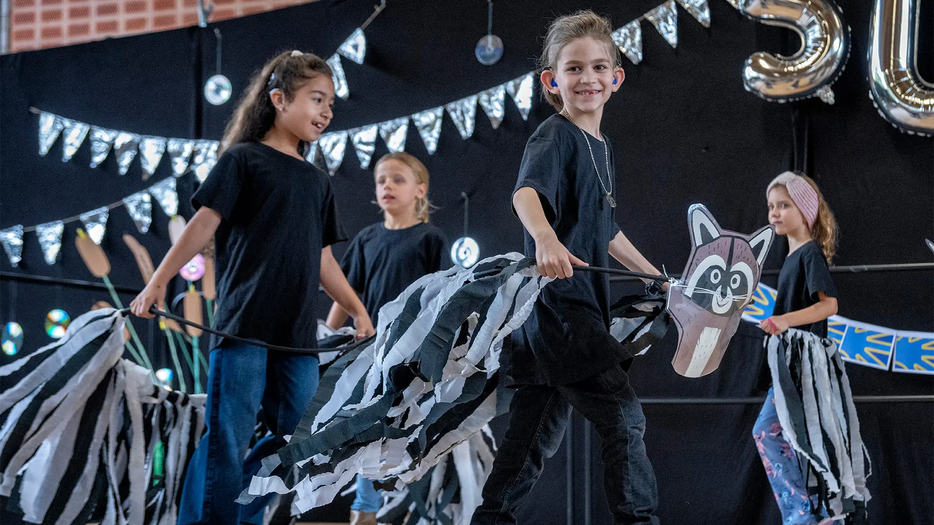 Vier Schüler*innen bei einer Performance auf der Bühne. Ein Schulkind schaut lächelnd in Richtung Kamera.