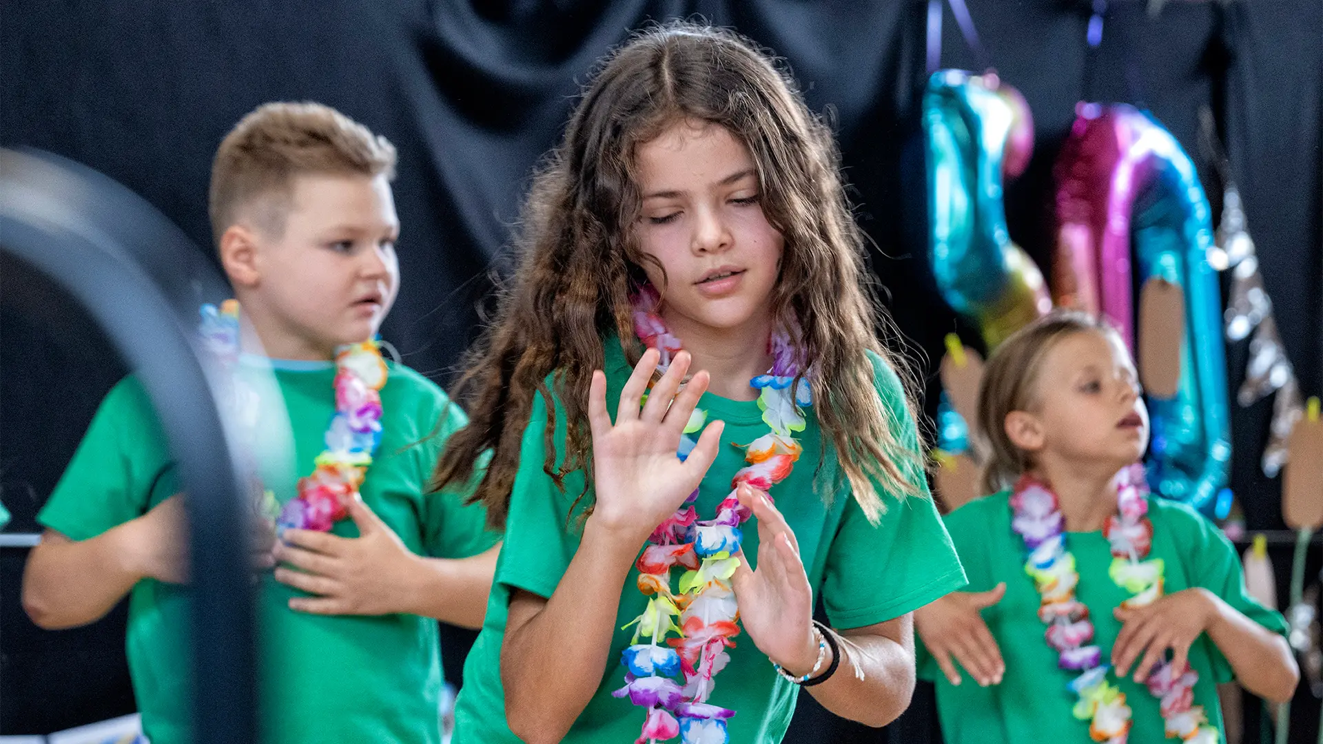Drei Schüler*innen bei einer Tanz-Performance. Sie tragen bunte Blumenketten.