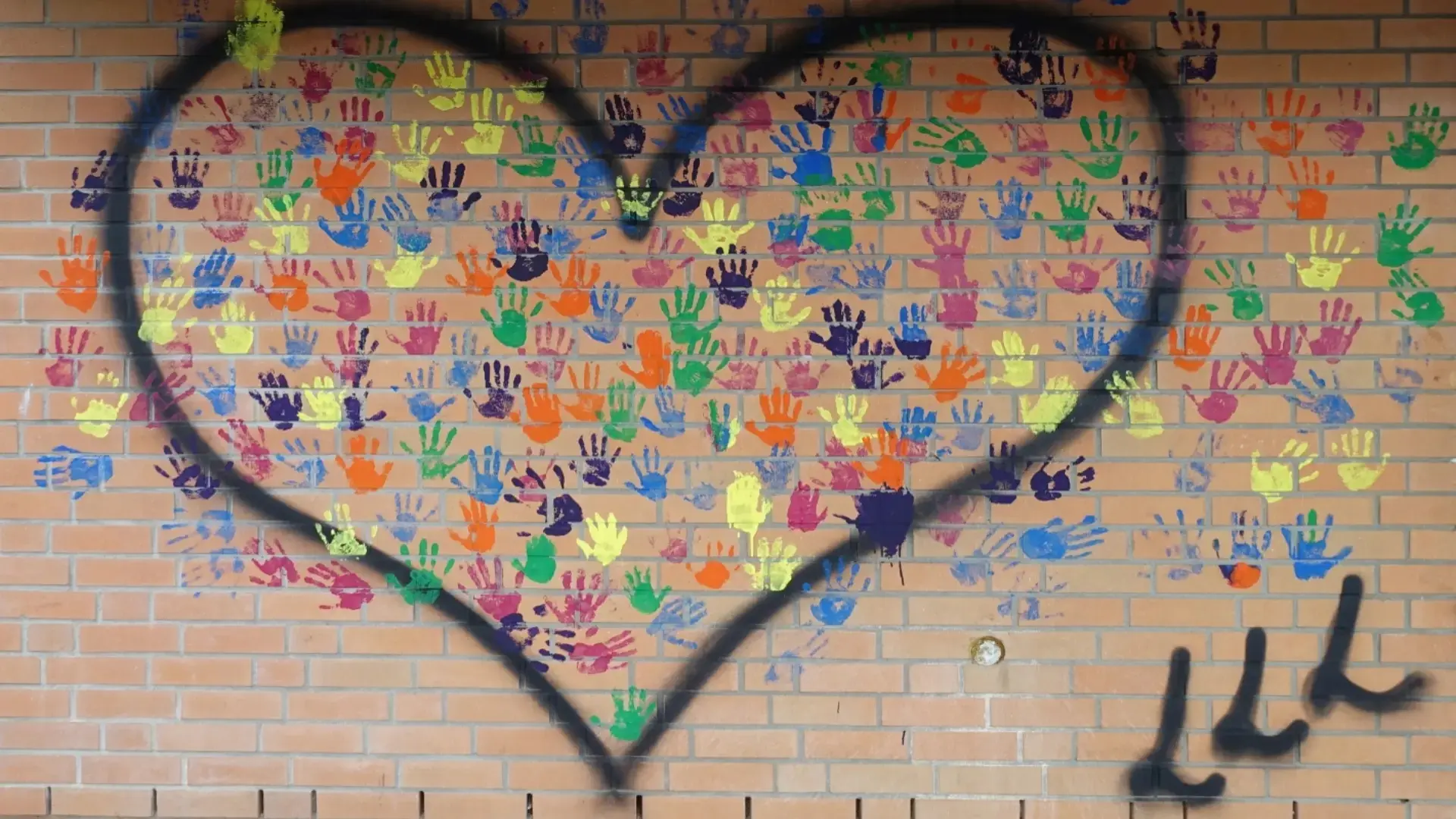 Viele bunte Handabdrücke im Herz auf der Wand mit Initialen der Schule