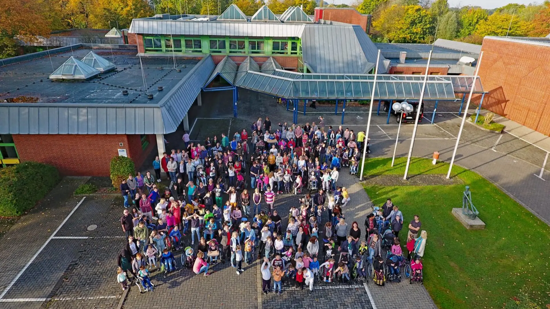 Blick von oben: Schüler*innen stehen auf dem Schulhof vor der Schule