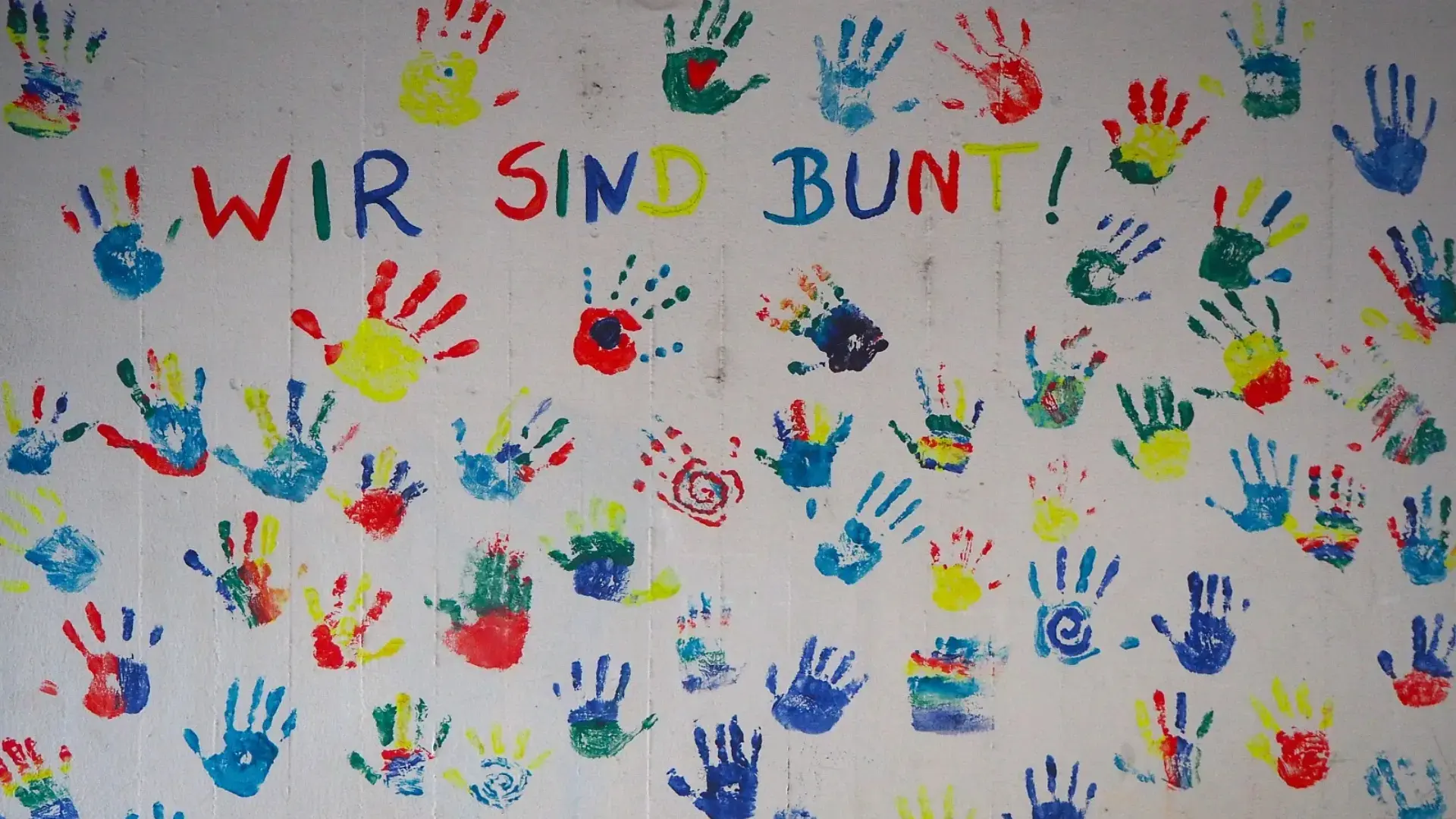 Wand mit vielen bunten Handabdrücken und der Aufschrift: "wir sind bunt!"