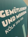 Blick auf ein Ausstellungsplakat mit dem Titel "Gemütlichkeit und Moderne. Köln 1918 bis 1926". 