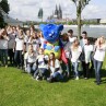 Junge Männer und Frauen in T-Shirts mit dem Aufdruck "Tag der Begegnung" posieren am Rheinufer mit dem LVR-Maskottchen Mitmän für ein Gruppenfoto.