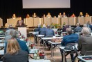 Foto einer Landschaftsversammlung, im Vordergrund sitzende Teilnehmer*innen der Versammlung von hinten, im Hintergrund ein langes leicht erhöhtes Podium, hinter dem die Vorsitzenden der Versammlun sitzen