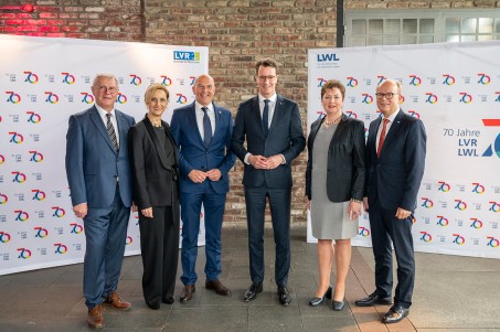 Sechs Personen stehen nebeneinander in einer Halle vor zwei Aufstellern mit dem Logo "70 Jahre LVR" und schauen in die Kamera