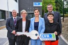 Drei Frauen und zwei Männer in formeller Kleidung halten einen überdimensionalen silbernen Schlüssel und das LVR-Logo in den Händen.