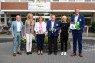 Mehrere Menschen stehen vor einem Krankenhaus und lachen in die Kamera. 