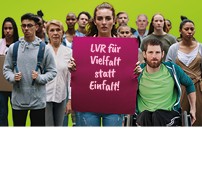 Gruppe aus Menschen verschiedenen Alters und Herkunft, Person in der Mitte der Gruppe hält ein Plakat hoch mit den Worten "LVR für Vielfalt statt Einfalt"