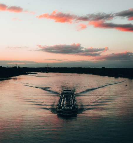 Blick auf den Rhein bei Bonn. In der Bildmitte ist ein Frachtschiff zu sehen, dass auf den Betrachter zufährt. Im fernen Hintergrund befindet sich die Kennedy-Brücke. Die Stimmung und Farbgebung sind abendlich-romantisch.