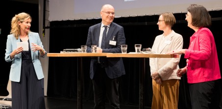 Vier Personen stehen an Stehtischen und blicken einander an.