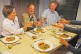 Foto: Menschen am Tisch mit Tellern vor sich. Sie stoßen an.