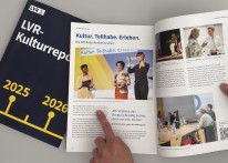 Eine Hand zeigt mit ausgetecktem Finger auf ein aufgeklapptes Buch mit vielen Bildern.