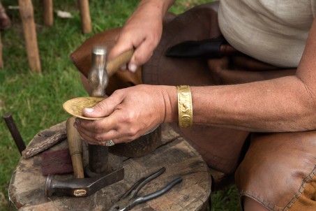 Ein Handwerker bearbeitet eine goldfarbene Platte mit dem Hammer