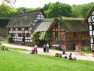 Foto: Blick auf historische Fachwerkgebäude, im Vordergrud eine grüne Wiese mit Menschen.