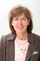 Eine Frau mit mittellangen braunen Haaren, einem brauen Jackett und einem hellrosa T-Shirt.