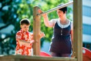 Ein kleiner blinder Junge tastet einen Balken ab, Teil eines Klettergerüstes auf dem Spielplatz. Seine Lehrerin steht daneben und gibt ihm Hinweise