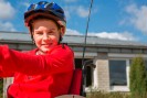 Ein Junge mit rotem Pulli sitzt in einem Handbike, trägt einen Helm und lächelt in die Kamera,