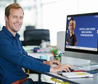 Ein Mann sitzt vor einem Computerbildschirm und schaut in die Kamera.