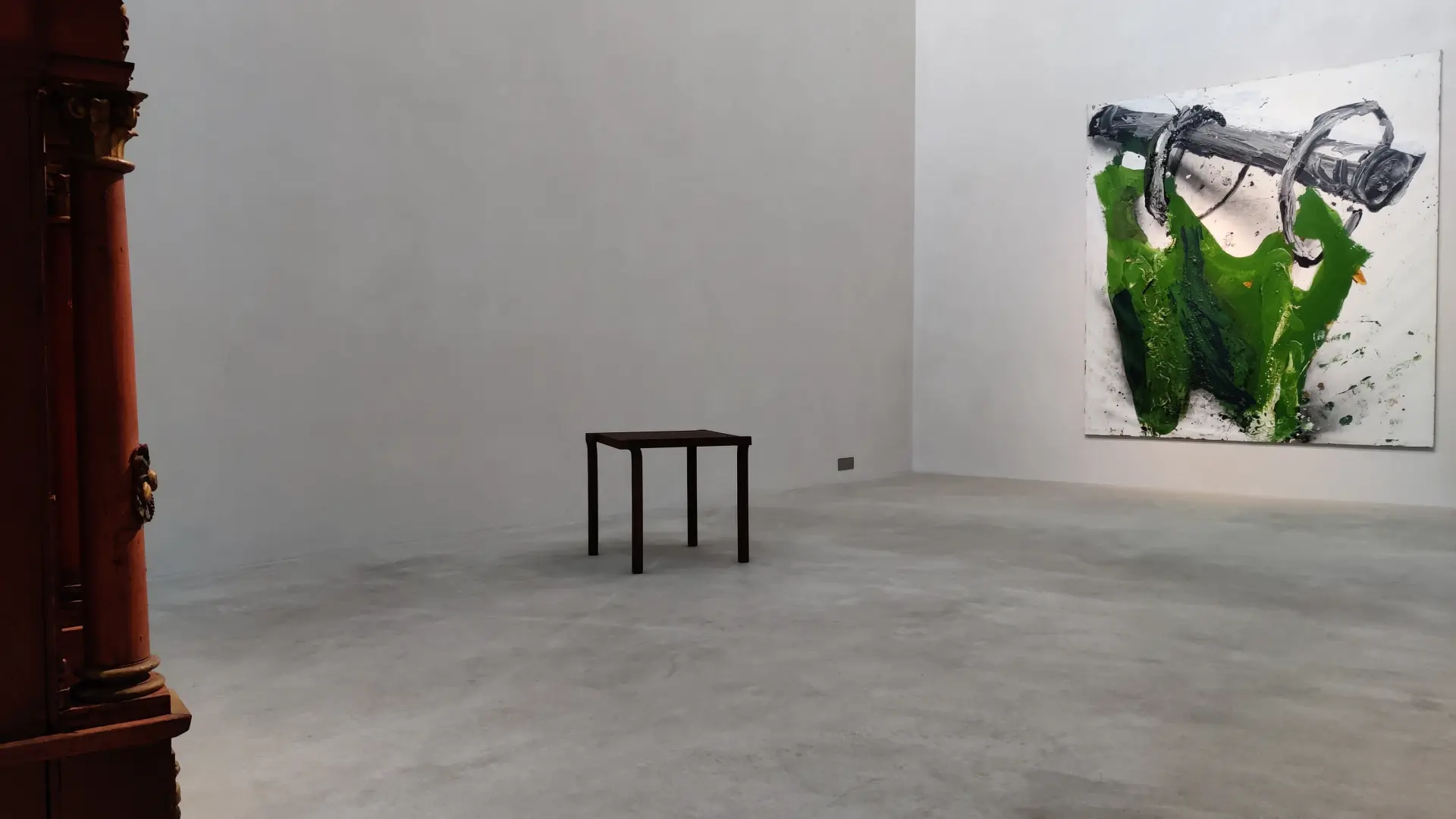 In einem Ausstellungsraum steht ein schwarzer Tisch.  An der Wand im Hintergrund ist ein modernes, grün-weißes Gemälde zu sehen.