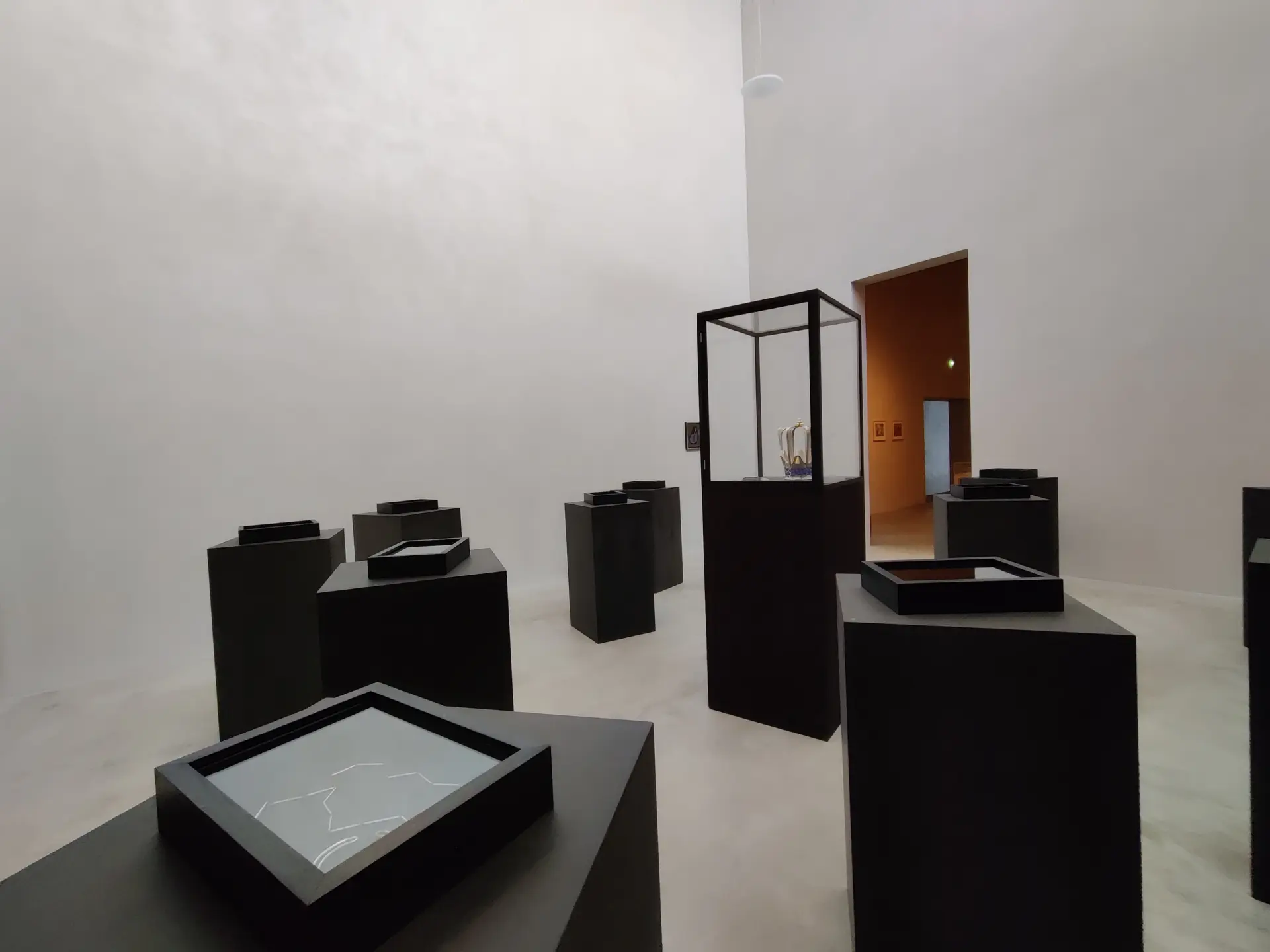 Ein weißer Raum in der eine schwarze Vitrine und mehrere schwarze Blöcke zu sehen sind, auf der Ausstellungsstücke stehen.
