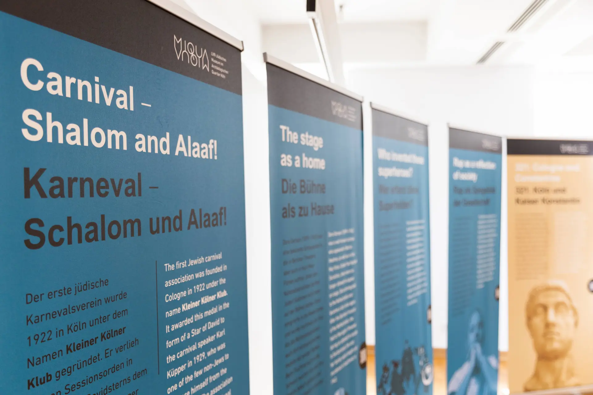 Nahaufnahme eines Handys, das von einer Person in der Hand gehalten wird, die den QR-Code eines Roll-ups der Posterausstellung scannt. Das blaue Roll-up ist im Hintergrund unscharf zu erkennen.