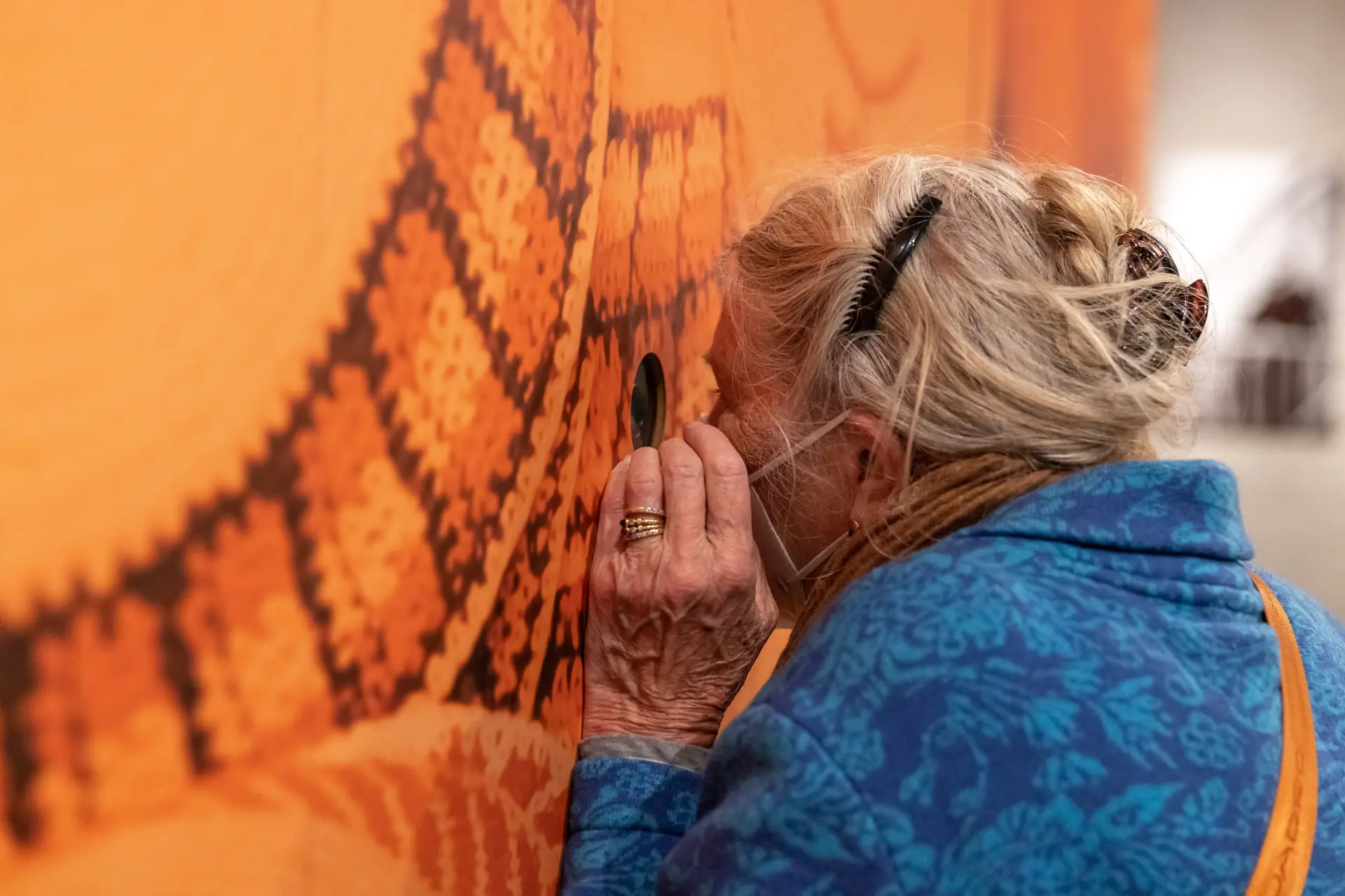 Eine Dame blickt durch ein Kuckloch in den orangenen Kubus rein.