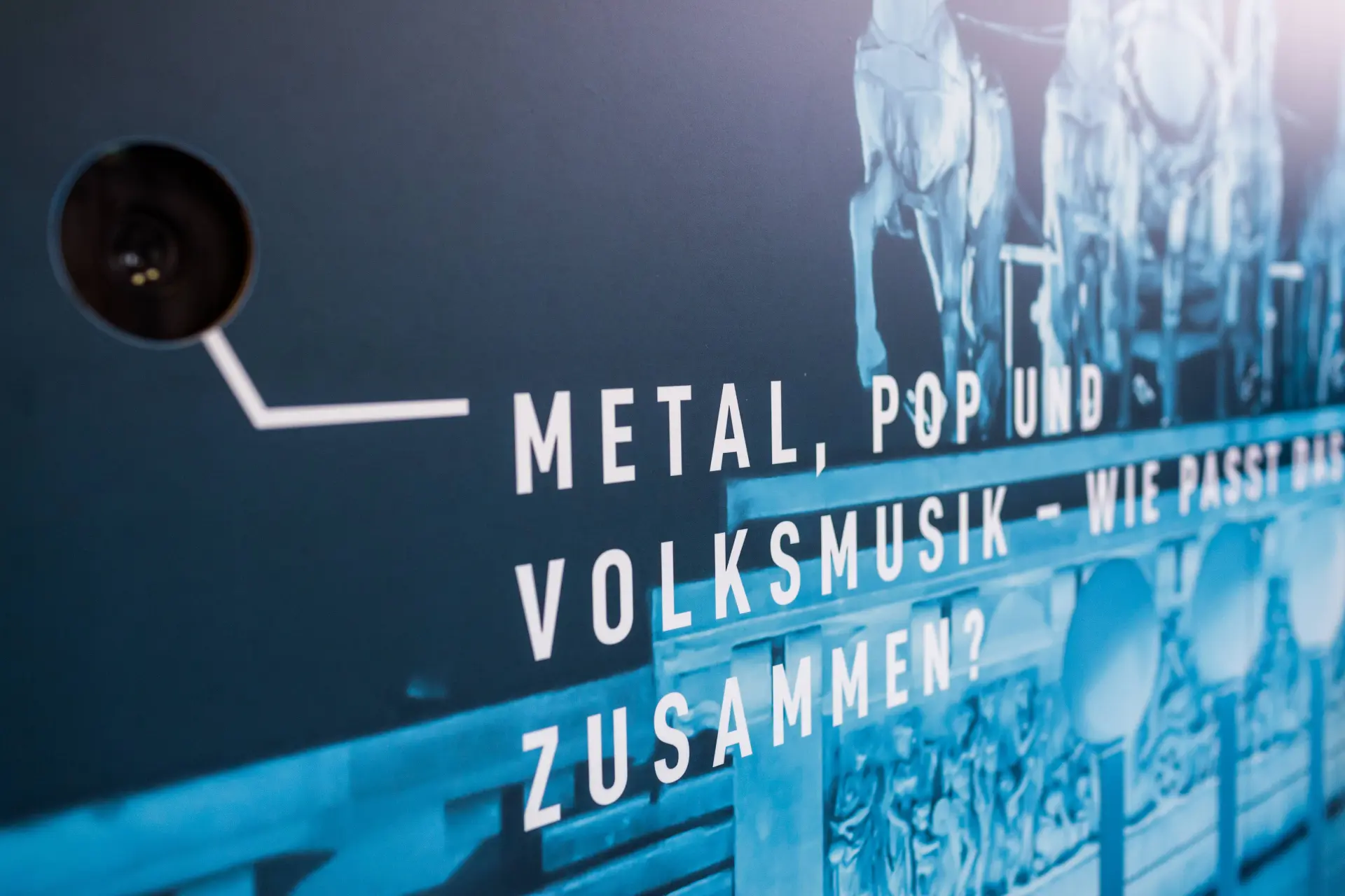 Eine Frau und zwei Männer stehen in dem Raum des Staatlichen Museum Ägyptischer Kunst, in dem die Ausstellungskuben platziert sind. Im Vordergrund ist eine Nahaufnahme von einem blauen Ausstellungskubus zu sehen, auf dem kostümierte Menschen erkennbar sind.