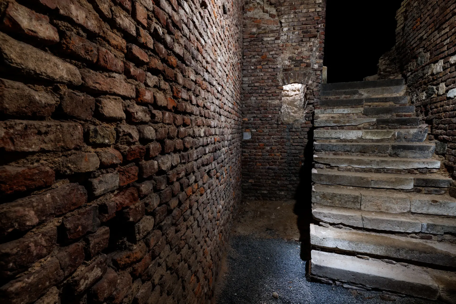Sandfarbene und rötlich Kellerwände aus Stein.  Eine Treppe führt noch oben.