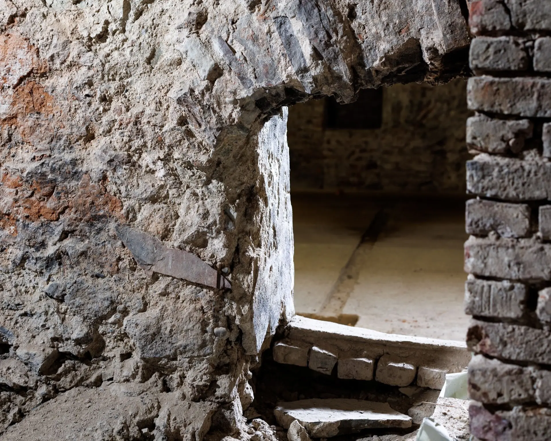 Eine Öffnung in einer Kellerwand lässt in den nächsten Raum einblicken.