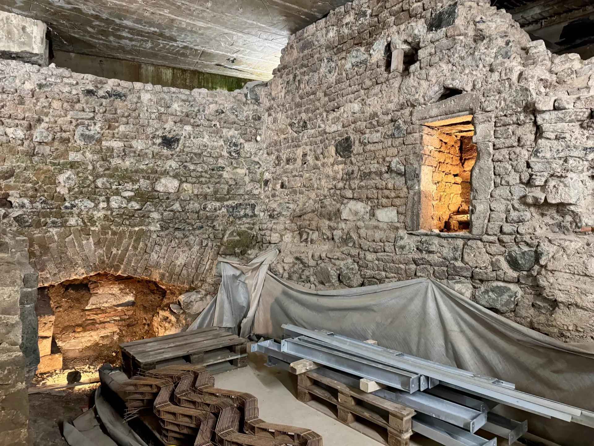 Sandsteinfarbene Kellerwände in der Ausgrabung des jüdischen Viertels.  Fensternischen sind mit Lichtern beleuchtet.