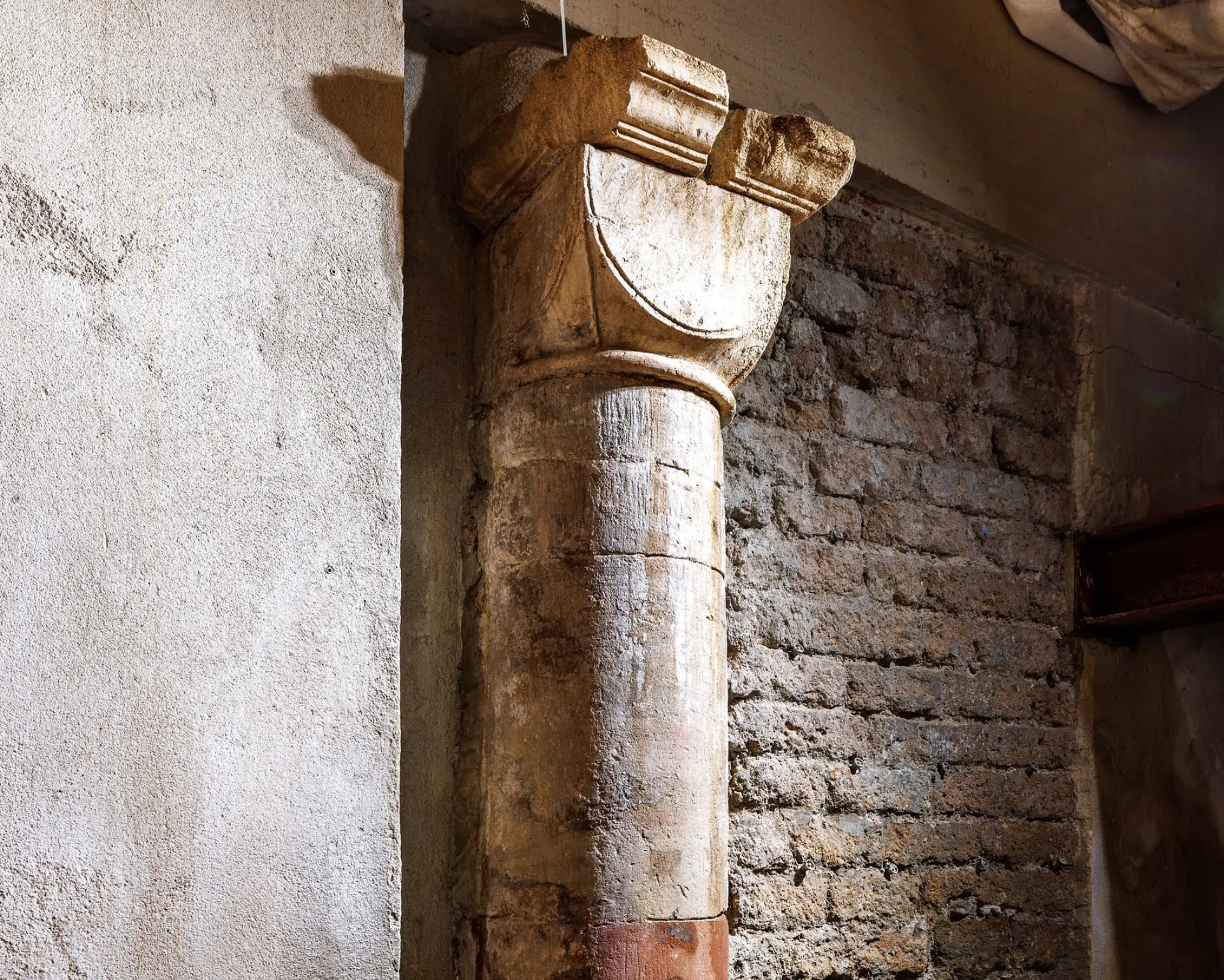 Eine sandfarbene Säule vor einer Backsteinwand.