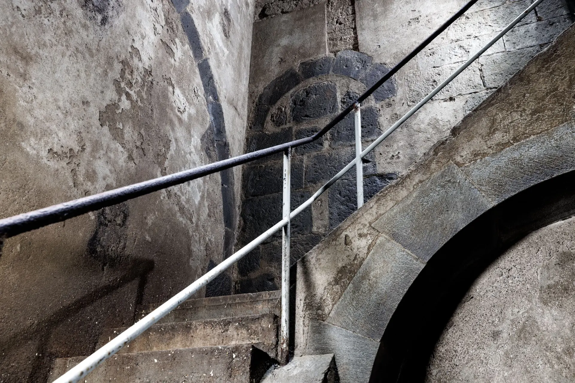 Ein Treppengeländer aus Metall führt eine Treppe aus Stein hoch.
