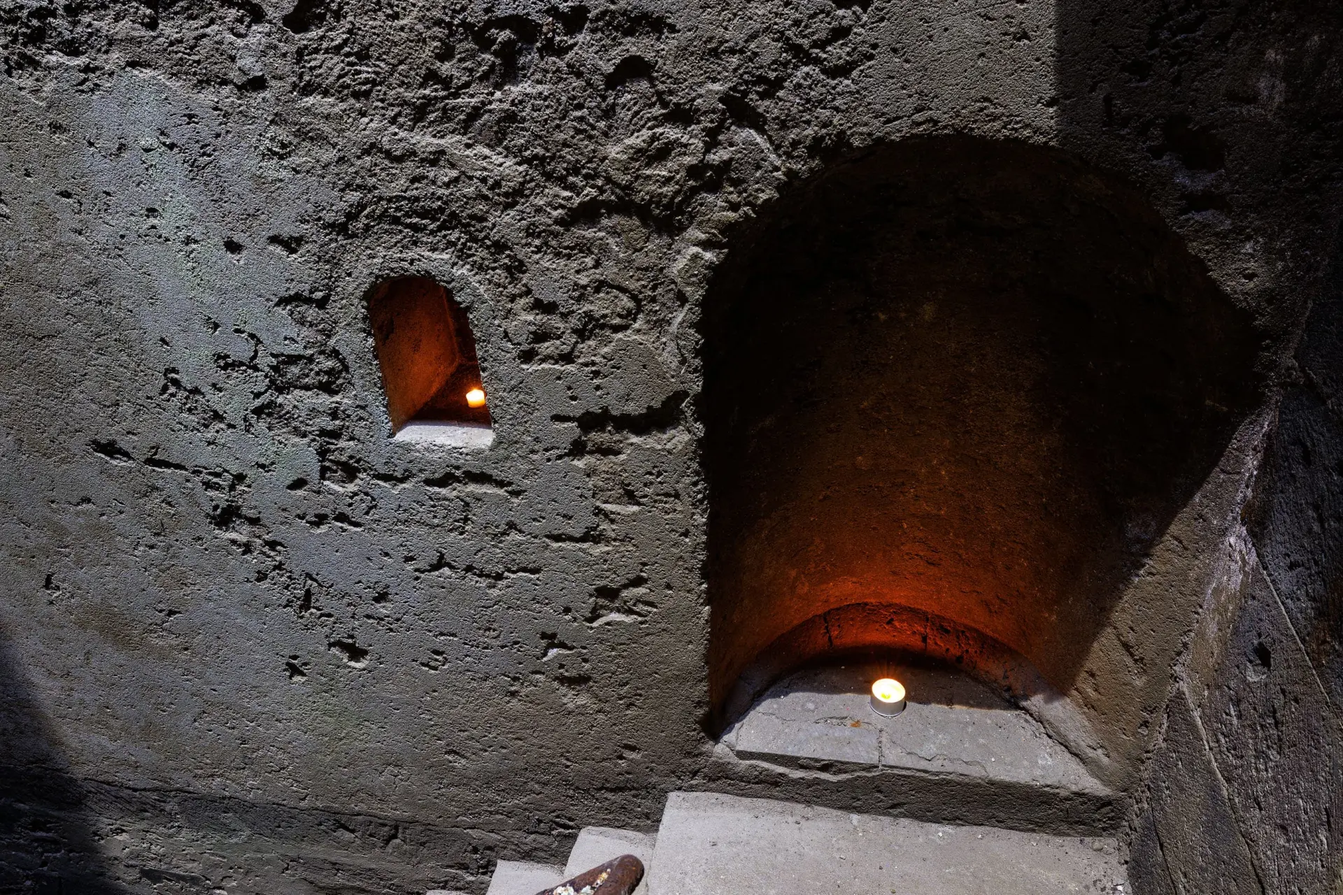 Eine Nische in einer grauen Wand ist mit einem Teelicht beleuchtet.