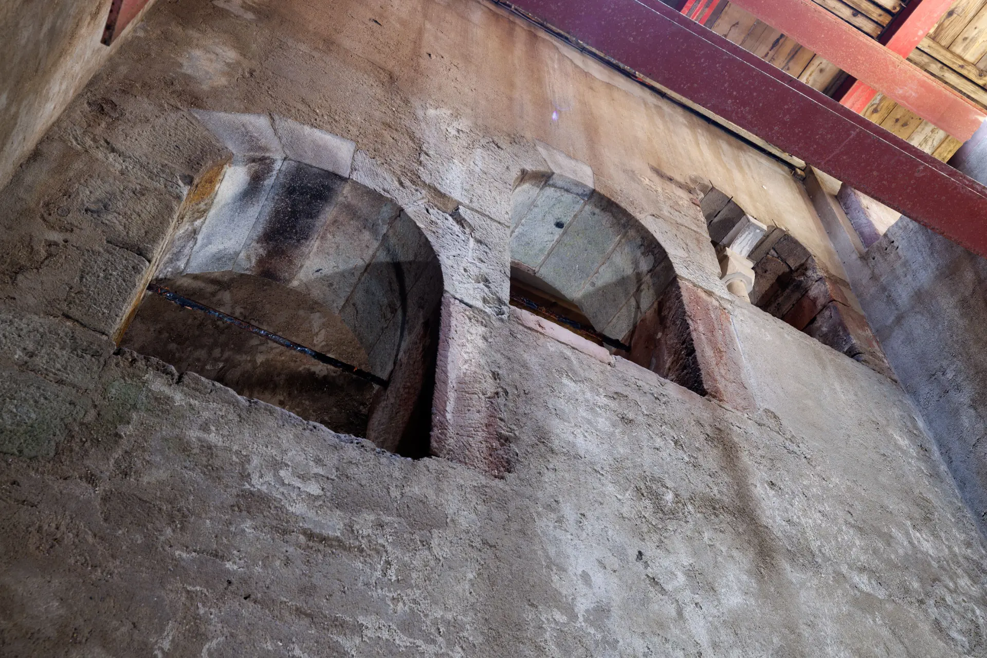 Ein Blick von unten nach oben auf eine graue Wand die mehrere Öffnungen mit Rundbögen zeigt.