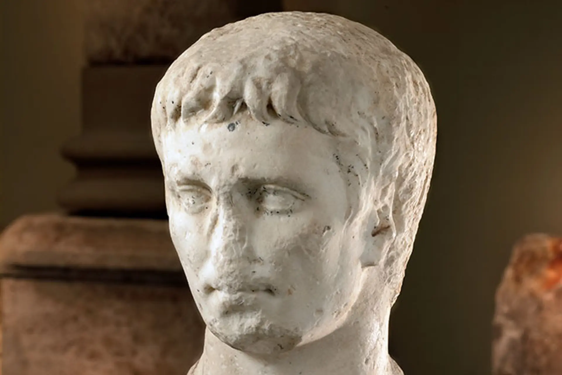 Büste von Kaiser Augustus. Es ist nur der Kopf der Büste zu erkennen, im Hintergrund dunkles Licht. 