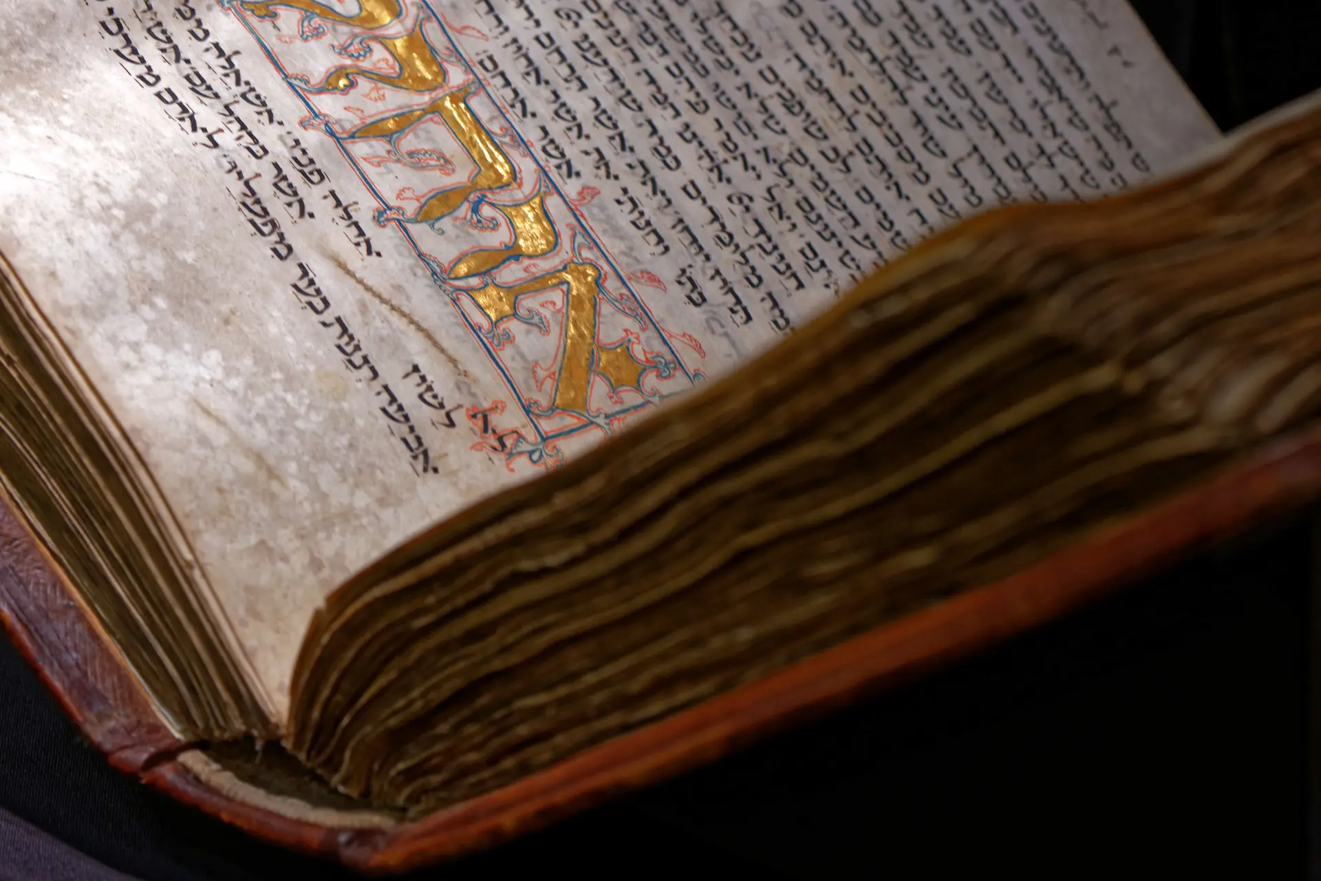 Hebräische Schrift in einem mittelalterlichen Buch, dem Amsterdam Machsor. Die hebräischen Schriftzeilen werden von kunstvollen Illuminationen und Schriftzügen in Blattgold ergänzt.