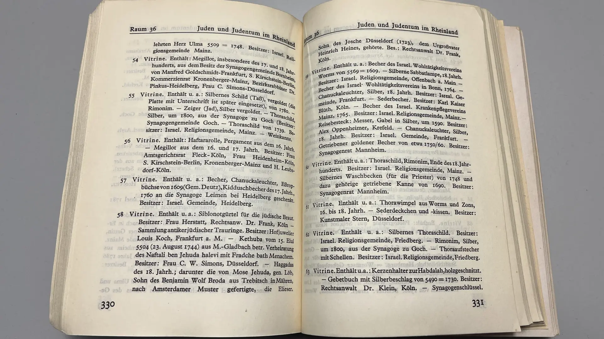 Nahaufnahme des Ausstellungskatalogs der Jahrtausend-Ausstellung, der aufgeschlagen auf einem Tisch liegt. Das Kapitel "Juden und Judentum in Rheinland" ist aufgeschlagen und zeigt eine Auflistung der Vitrinen mit Judaika-Objekten.