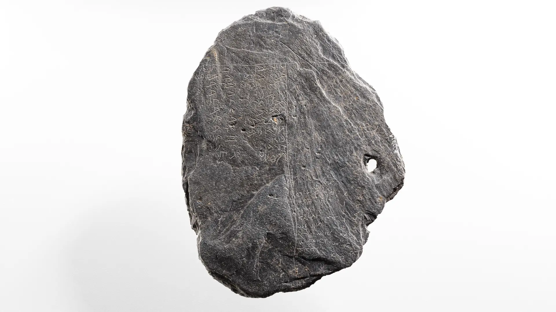 Ein Stück einer schwarzen Schiefertafel, in die hebräische Zeichen eingeritzt sind.