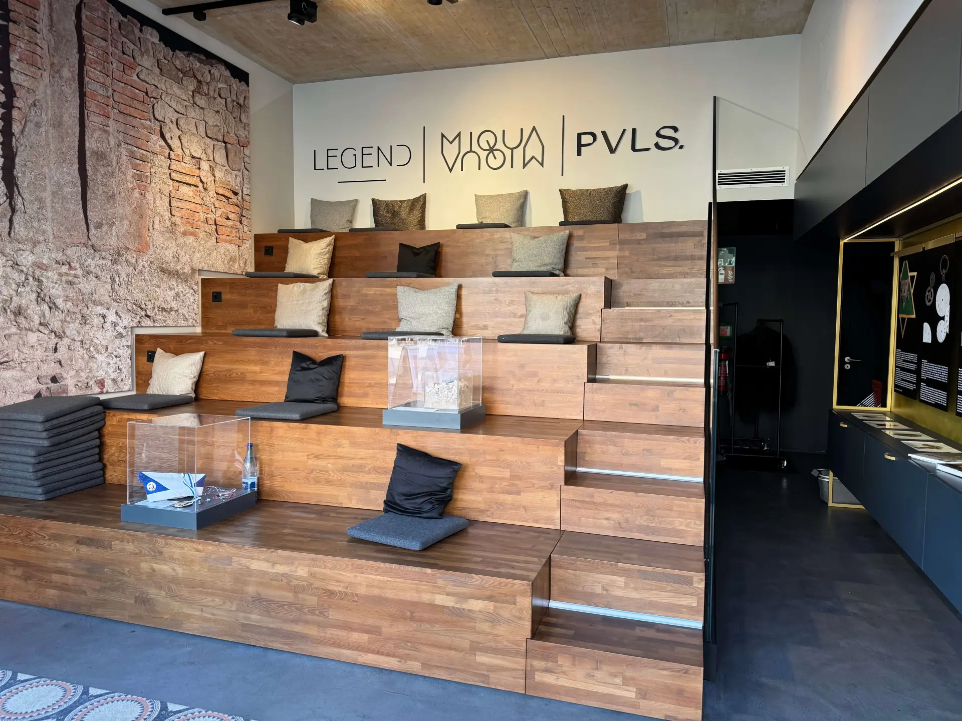 Ein silbernes Metallschild hängt an einer roten Außenwand.  Darauf steht MiQua:forum.