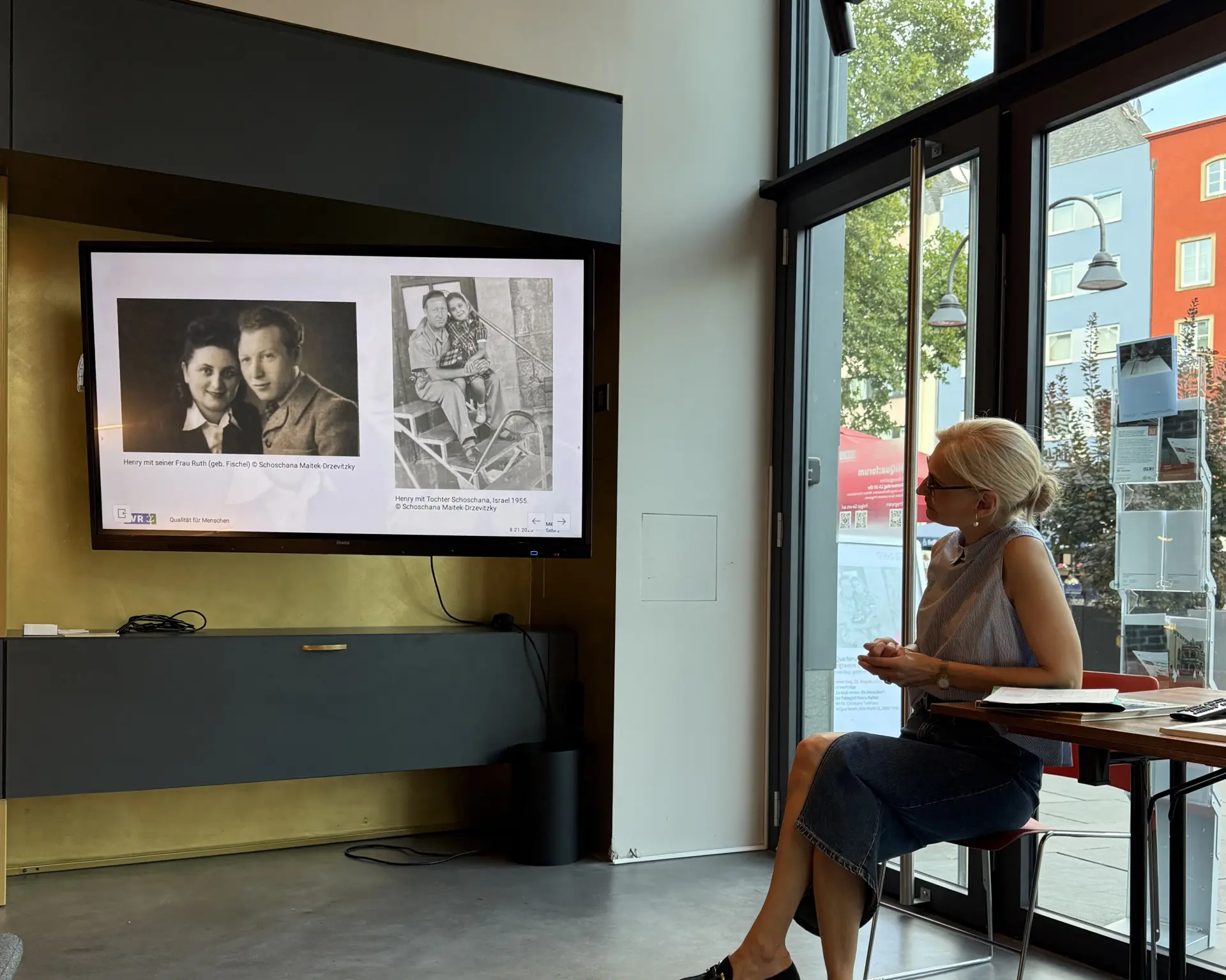 Eine Gruppe Menschen sitzt auf einer Treppe in einem Raum und schaut einem Vortrag zu.